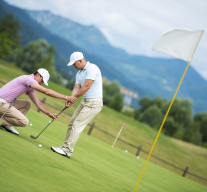 Golf pro teaching male golfer on putting green.