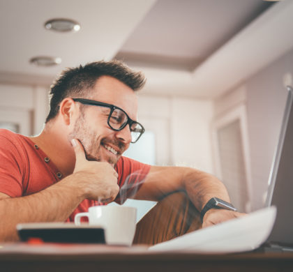 Man in red shirt smiling and using laptop at office