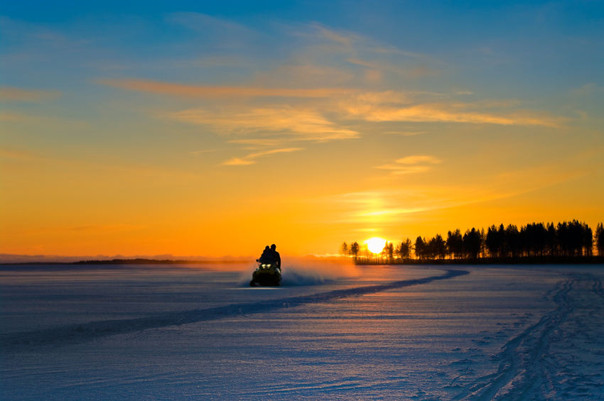 Blue and orange sunset on winter snowy lake and snowmobile with people on it.