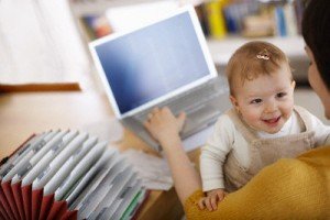 Woman Using a Laptop While Taking Care of Baby